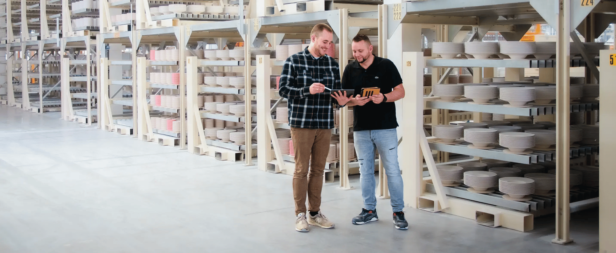 Zwei Herren stehen in einem Hochregallager und schauen auf ein Tablet