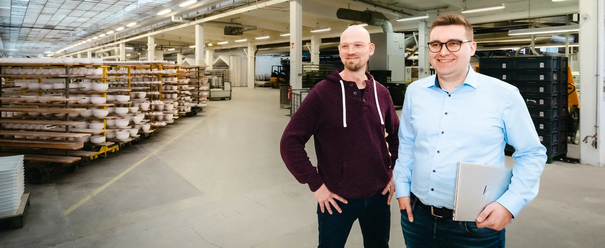 Ein IT-Mitarbeiter steht mit Laptop unter dem Arm beim Kunden in der Produktionshalle