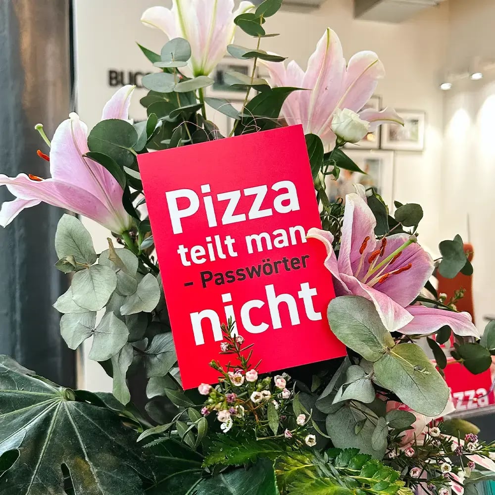 Ein Blumenstrauß mit Grußkarte auf der steht: Pizza teilt man – Passwörter nicht