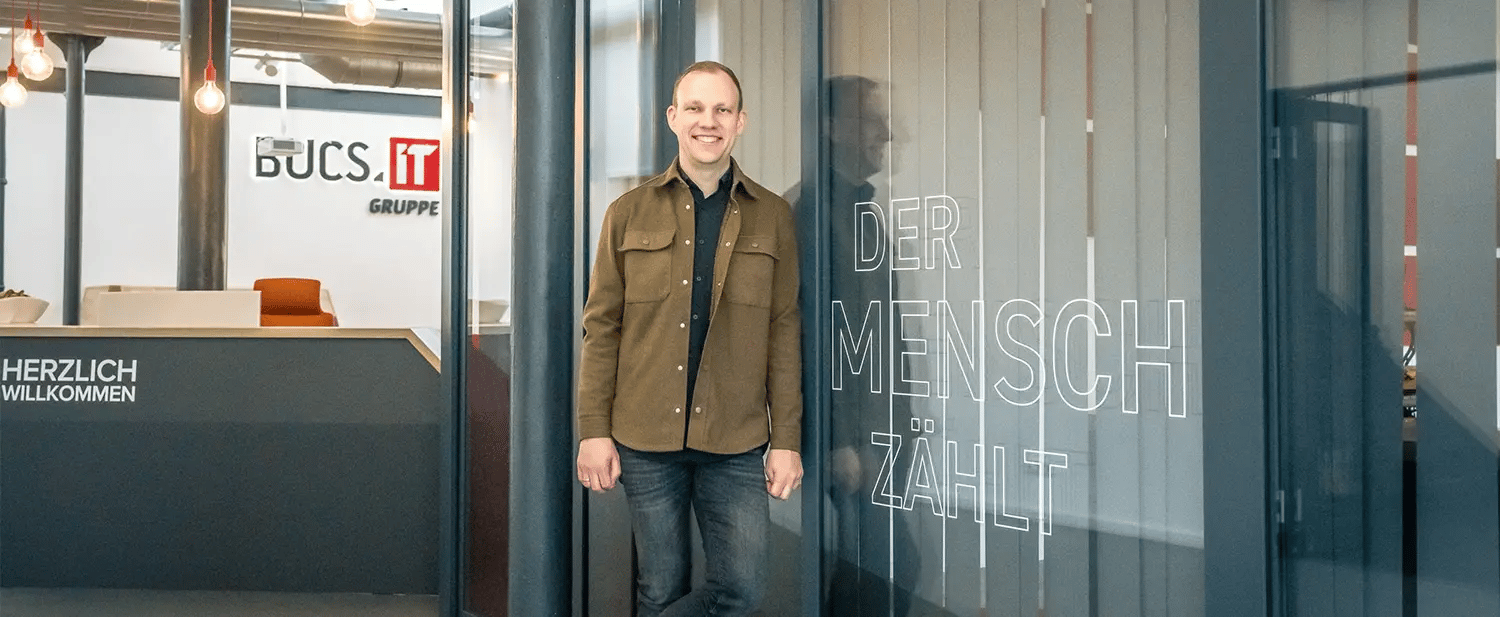 Ein Mann steht vor einer gläsernen Wand und lächelt in die Kamera