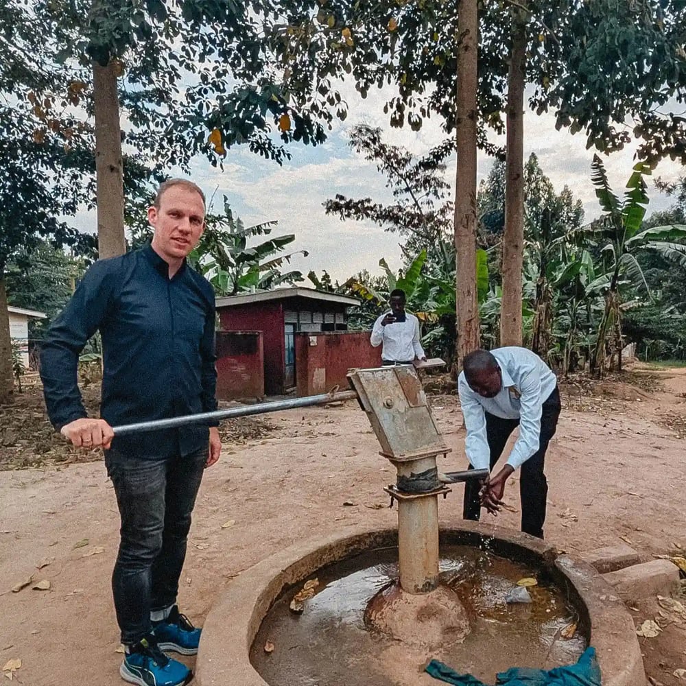 Ein Mann steht an einem Brunnen in Afrika und pumpt Wasser