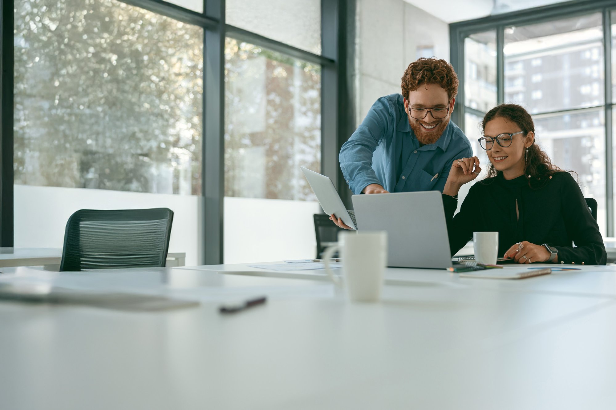 Zwei Menschen schauen gemeinsam auf einen Laptop in einem hellen Büro.