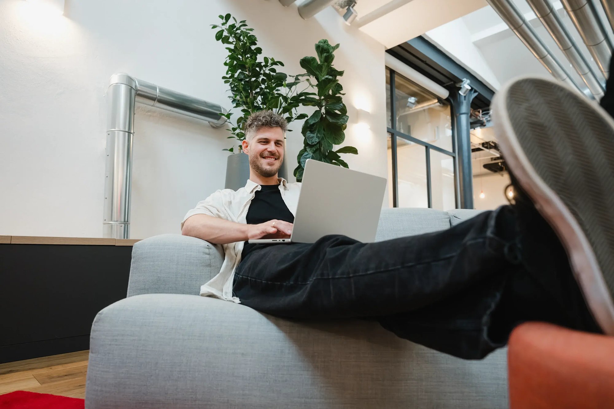 Ein Mann arbeitet an einem Laptop mit Cloud Speicher auf einer Couch im Büro
