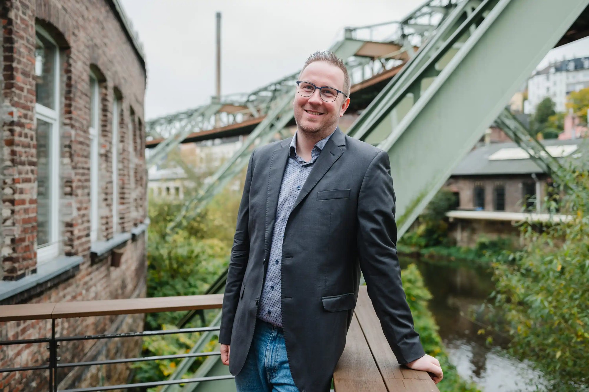 Freundlicher IT-Berater steht auf einer Veranda unter der Schwebebahn