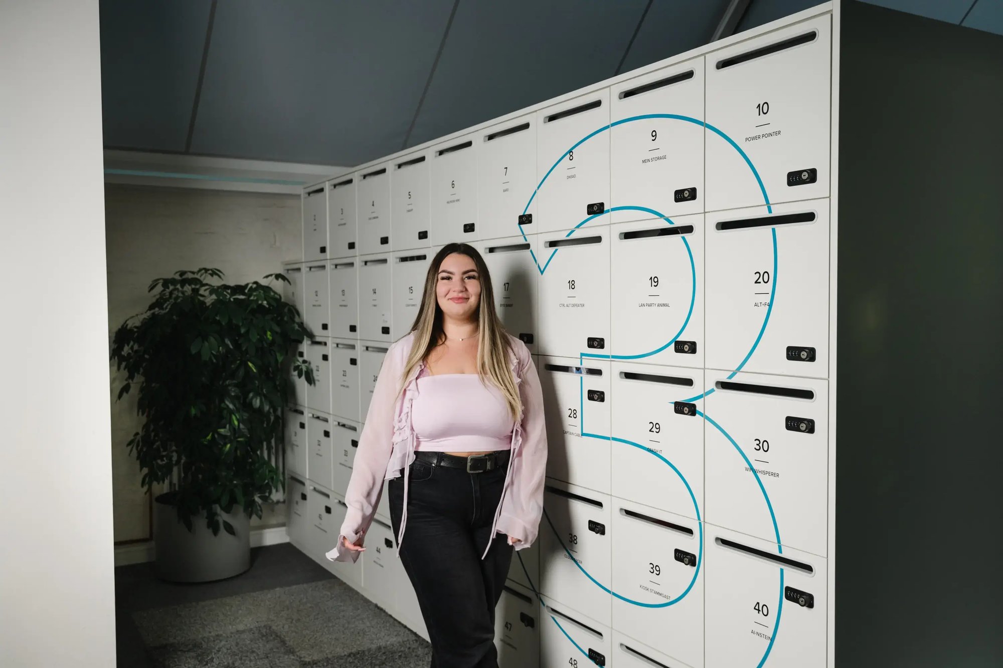 Mitarbeiterin steht vor Schließfächern und Pflanze